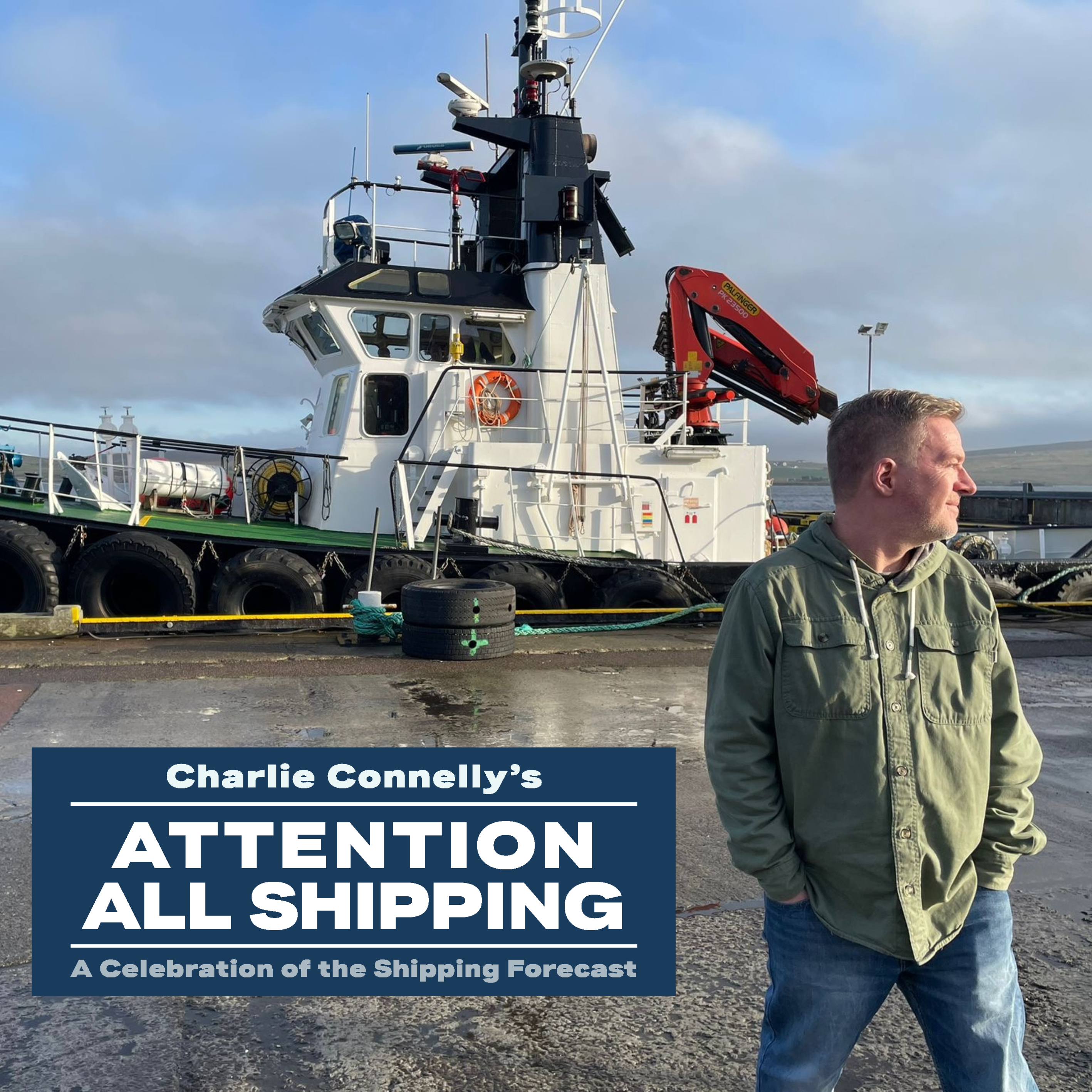 Charlie Connelly at a shipyard infront of a white and ship.  Charlie Connelly who is presenting the event Attention All Shipping A Celebration of the Shipping Forecast at the Victoria Theatre Halifax is wearing a green top and blue jeans