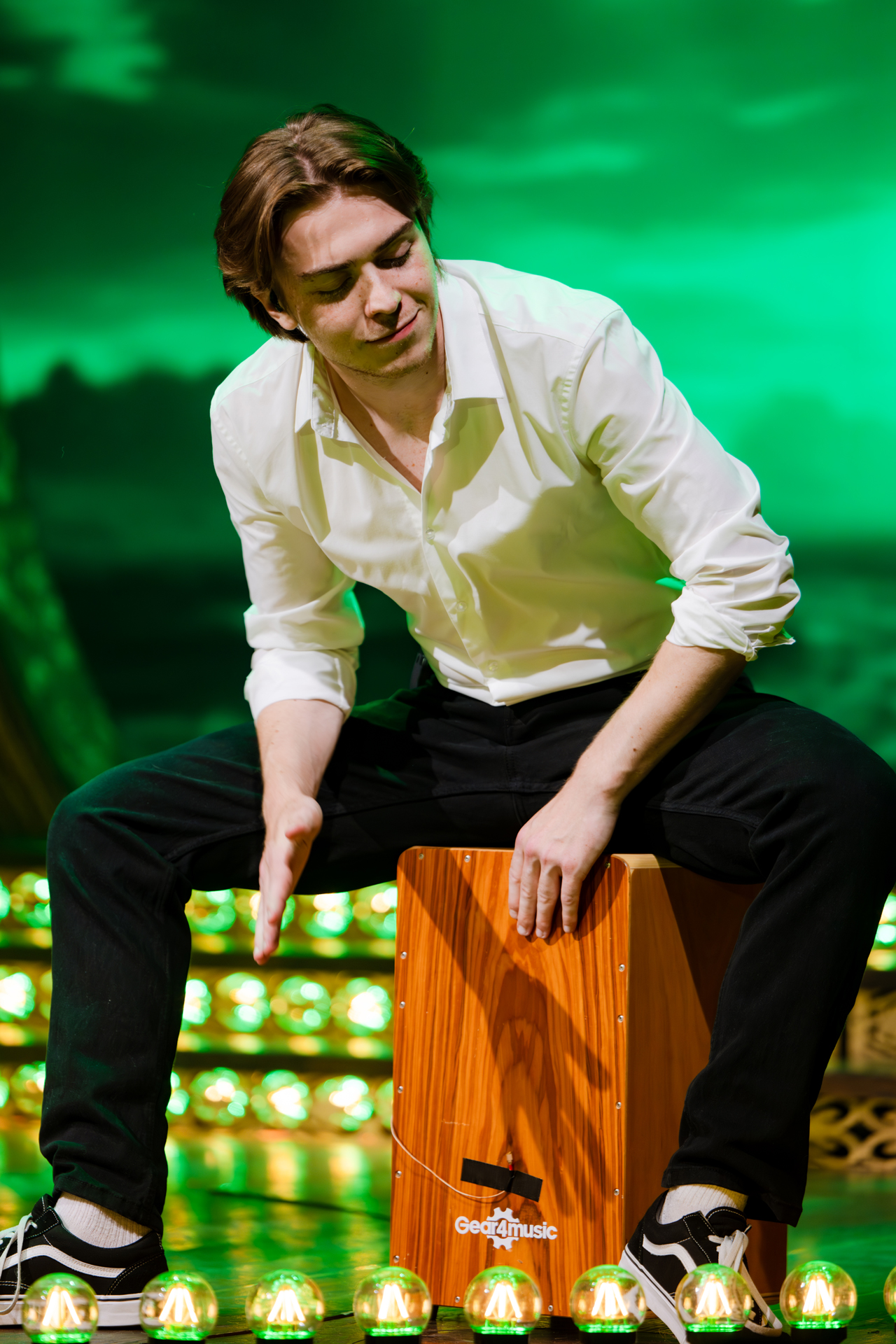A man beating a wooden box on stage for the event Adam Garcia's Emerald Storm