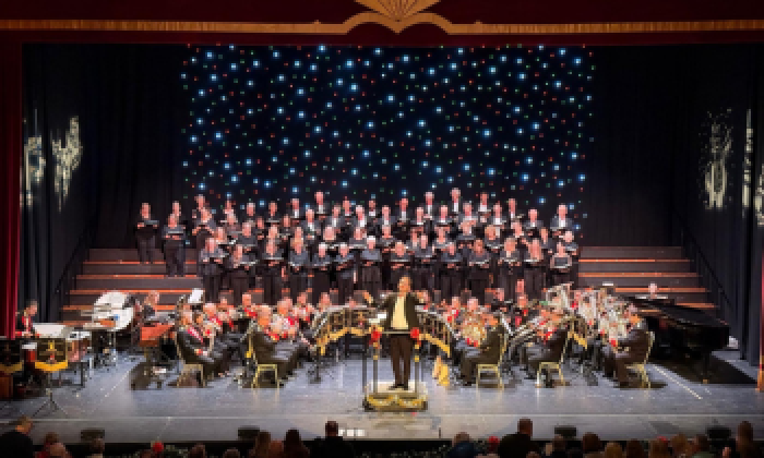 The Halifax Choral Society and Black Dyke Band live on stage at The Victoria Theatre facing the conductor as part of the Carols and Brass event